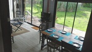 A dining area with a table set for two, a TV, and a grill outside. - Gîte de Linxe - Linxe (LINXE)