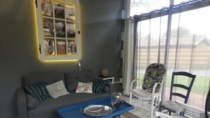 A cozy living room with a grey sofa, a blue coffee table, and a white chair with a floral cushion. - Gîte de Linxe - Linxe (LINXE)