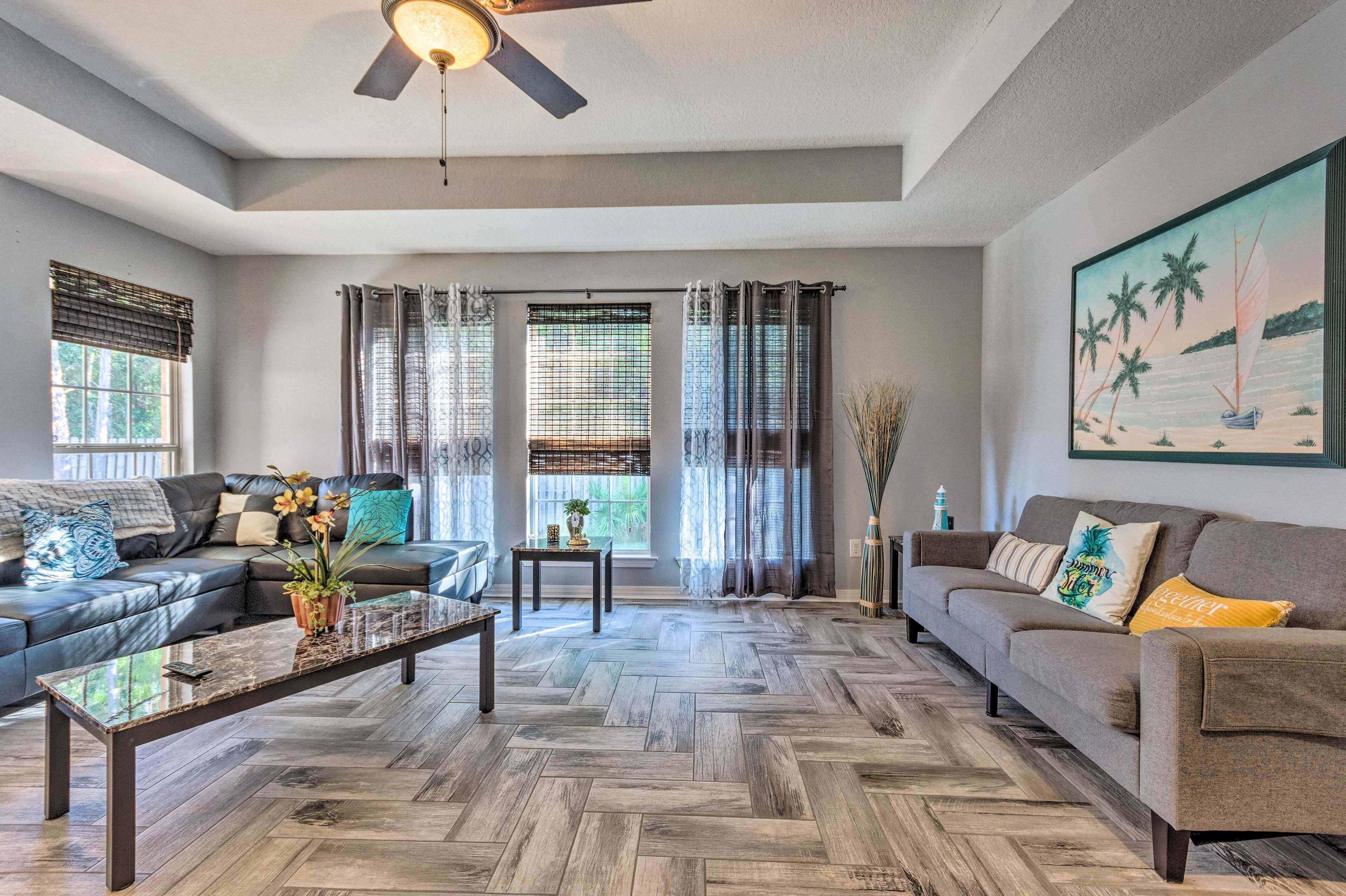 Un salon doté d’un parquet en chevrons, de deux canapés, d’une table basse et d’un ventilateur de plafond.