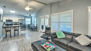 A modern kitchen with stainless steel appliances, a dining area with a black chair, and a living room with a leather sofa and a green throw pillow. - Pensacola Home - 2 Blocks From Boat Launch! (Pensacola)