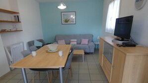 A modern living room with a wooden dining table, grey sofa, and a TV on a wooden cabinet. - Marensin - Mugron - Gîte (MUGRON)