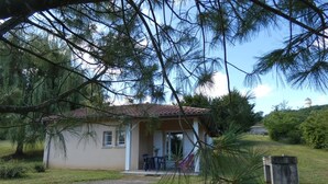 A small, single-story building with a tiled roof, a porch with a table and chairs, and a grassy yard. - Marensin - Mugron - Gîte (MUGRON)