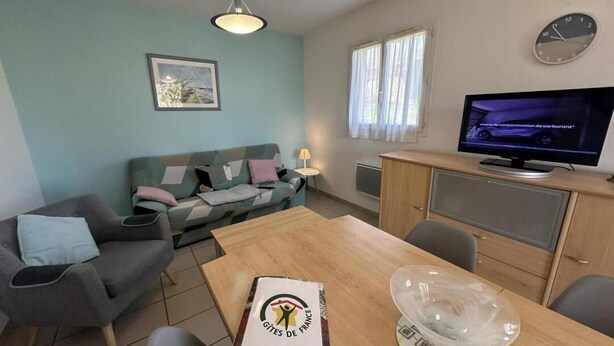 A cozy living room with a sofa, a dining table, and a television. - Marensin - Mugron - Gîte (MUGRON)