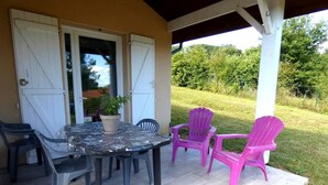 An outdoor patio with a table and chairs, a potted plant, and a view of a grassy area. - Marensin - Mugron - Gîte (MUGRON)