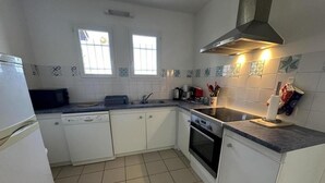 A compact kitchen with white cabinets, a stove, a dishwasher, and a window with bars. - Marensin - Mugron - Gîte (MUGRON)