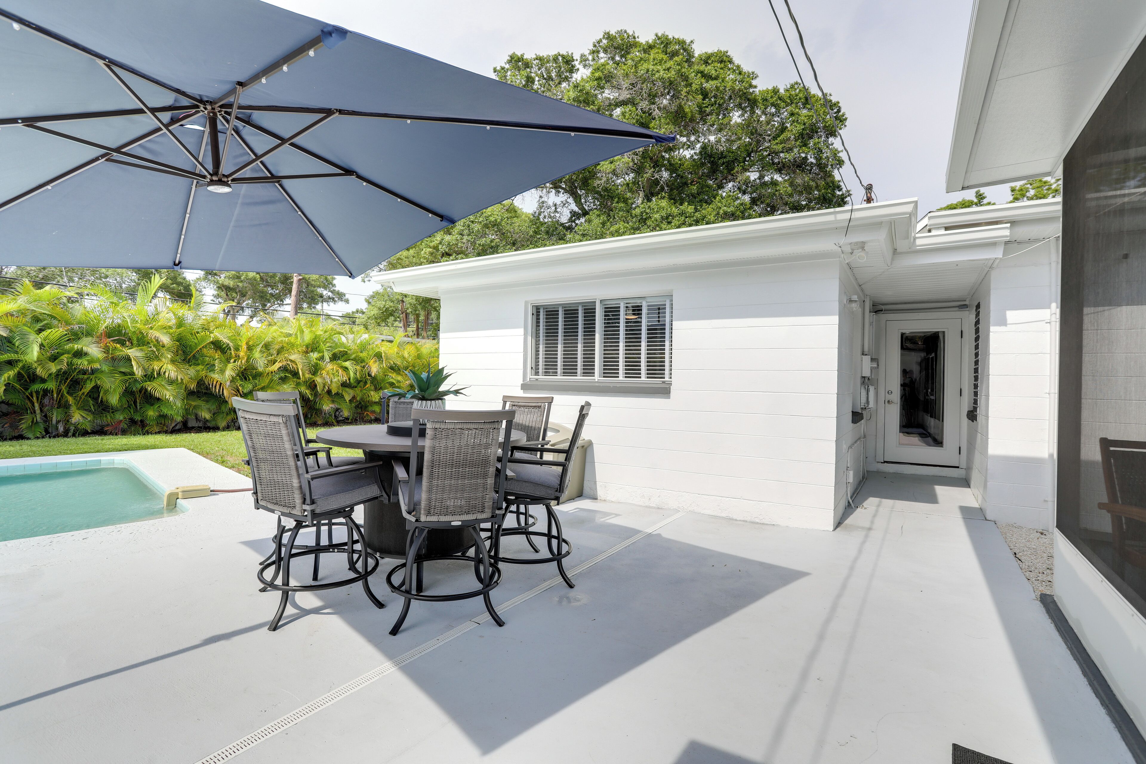 A patio with a pool, outdoor furniture, and a large umbrella.