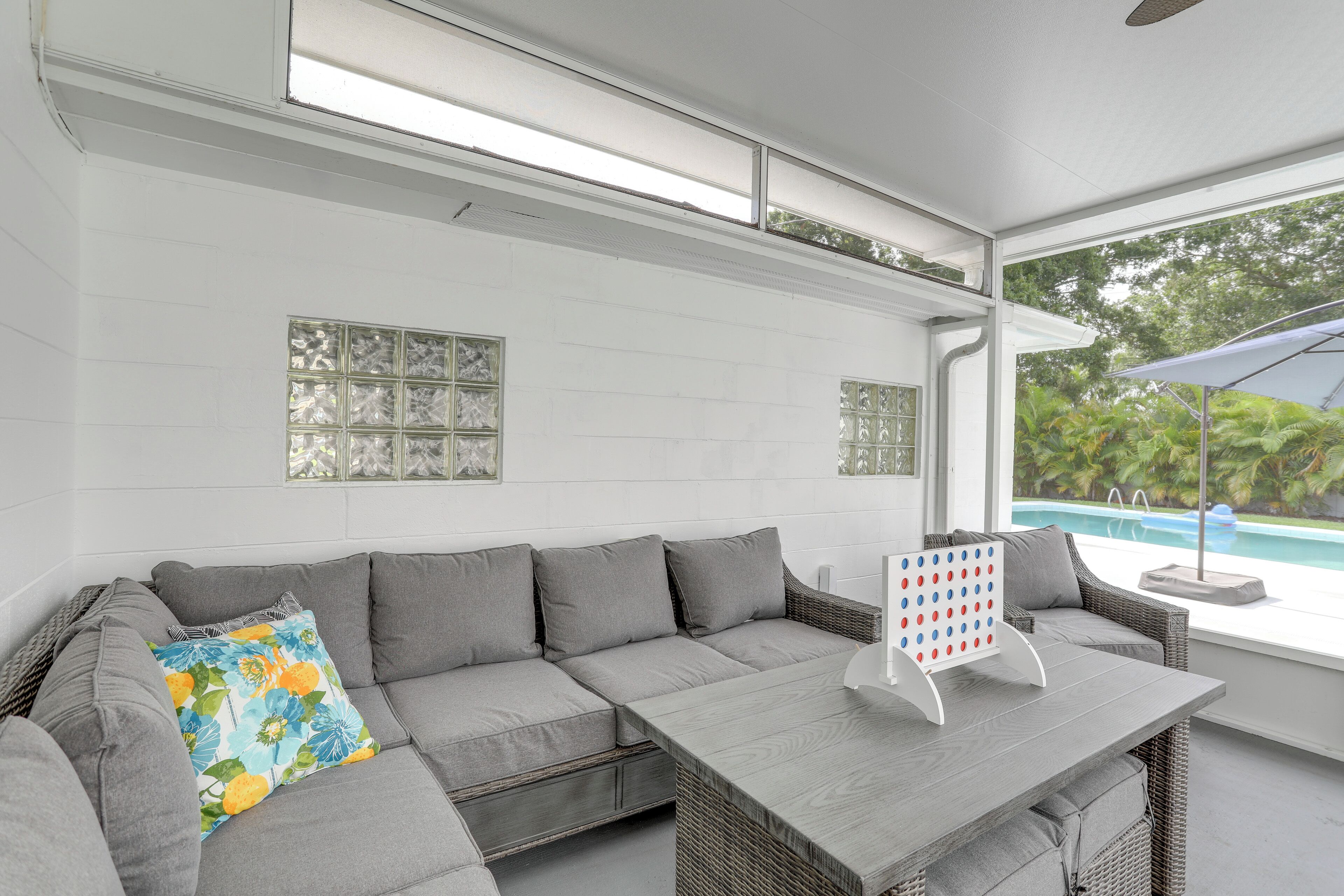 A modern outdoor seating area with a grey sofa, a wooden table, and a view of a swimming pool.