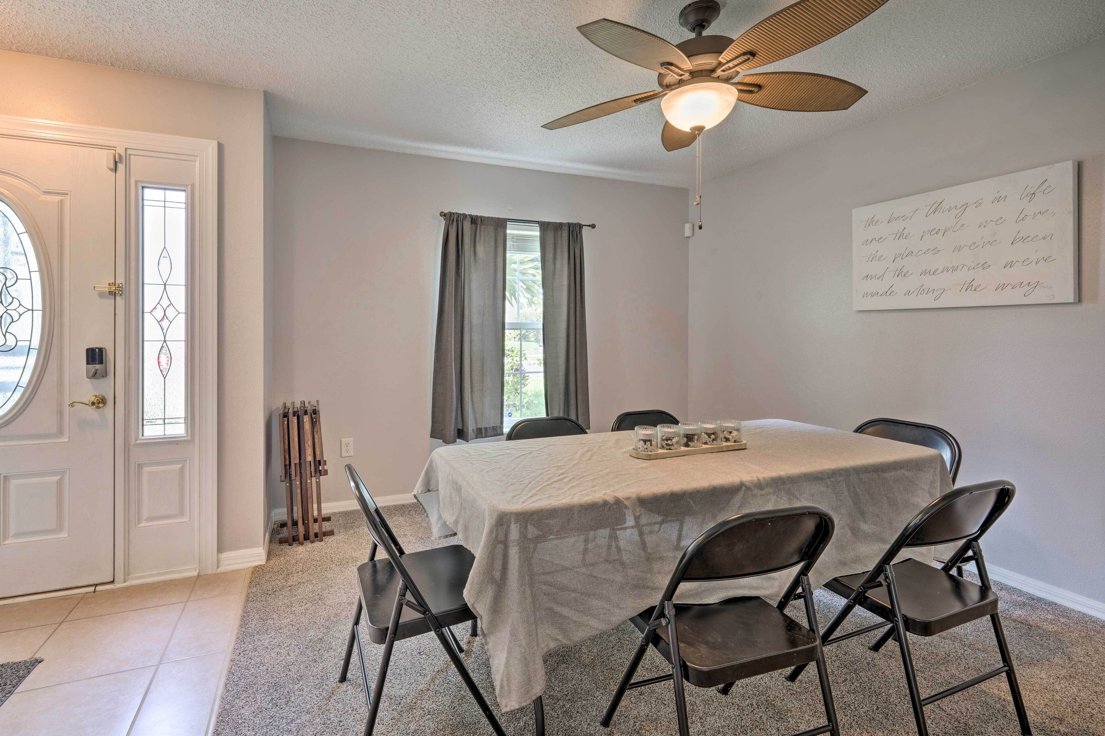 A dining room with a table set for four, chairs, a ceiling fan, and a view through a window.