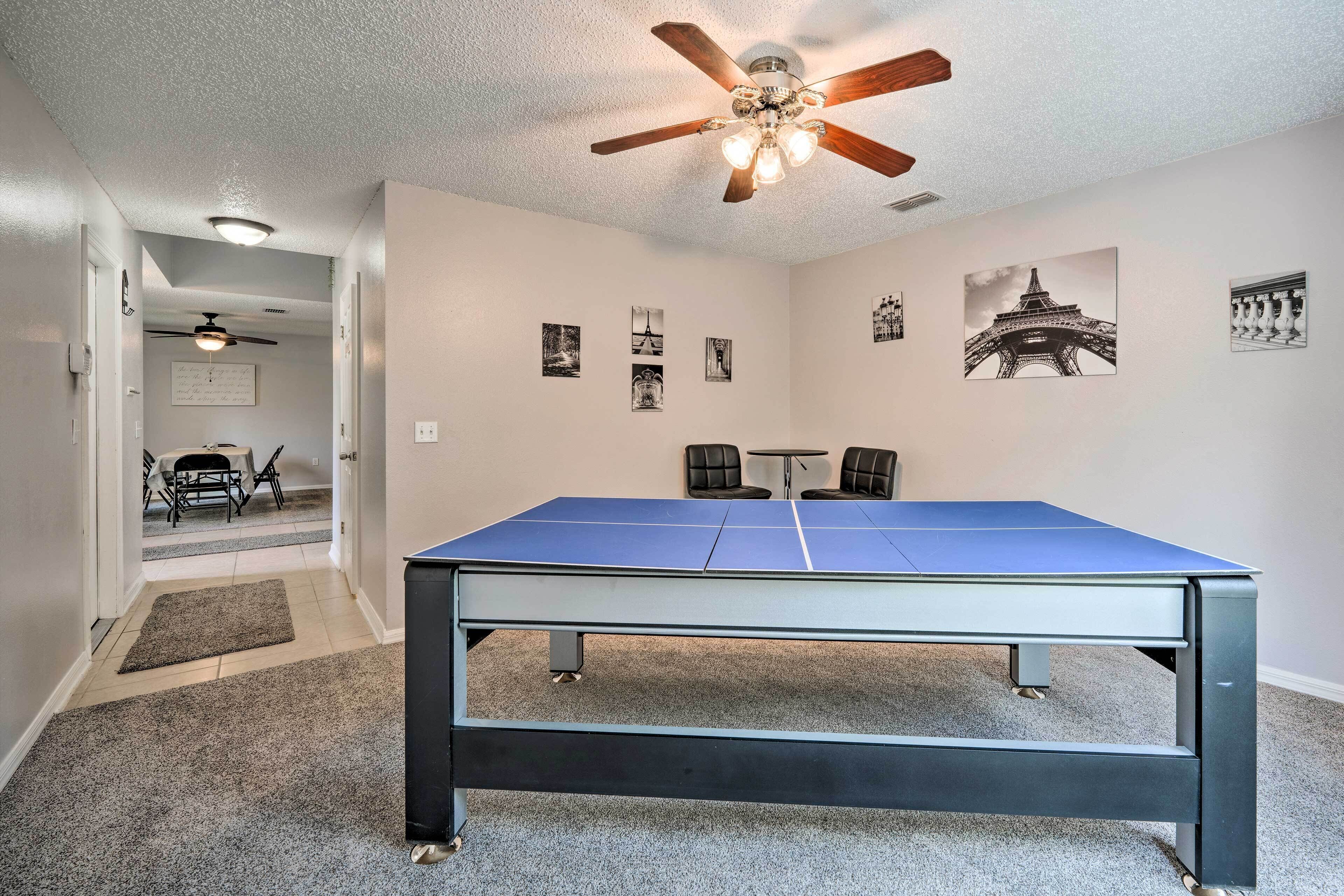 A room with a ping pong table, ceiling fan, and wall art including the Eiffel Tower.