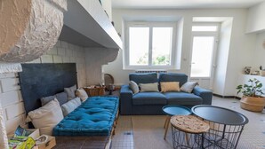 A cozy living room with a blue sofa, a dark-colored couch, and a small round table. There is a brick wall on one side and a large window providing natural light. - Gîte Capérot - Eyres Moncube (EYRES MONCUBE)