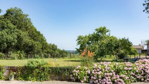 A garden with a variety of plants and trees, a gravel path, and a building in the background. - Gîte Capérot - Eyres Moncube (EYRES MONCUBE)