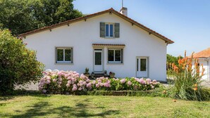 A white house with a tiled roof, two windows with shutters, and a small porch. - Gîte Capérot - Eyres Moncube (EYRES MONCUBE)
