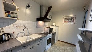 A compact kitchen with white cabinets, a sink, a stove, and a microwave. There is a small refrigerator and a kettle on the counter.