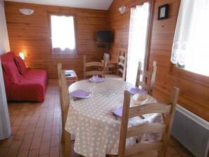 Cozy dining area with a round table and comfortable seating for six, featuring a lounge chair and a mounted television.