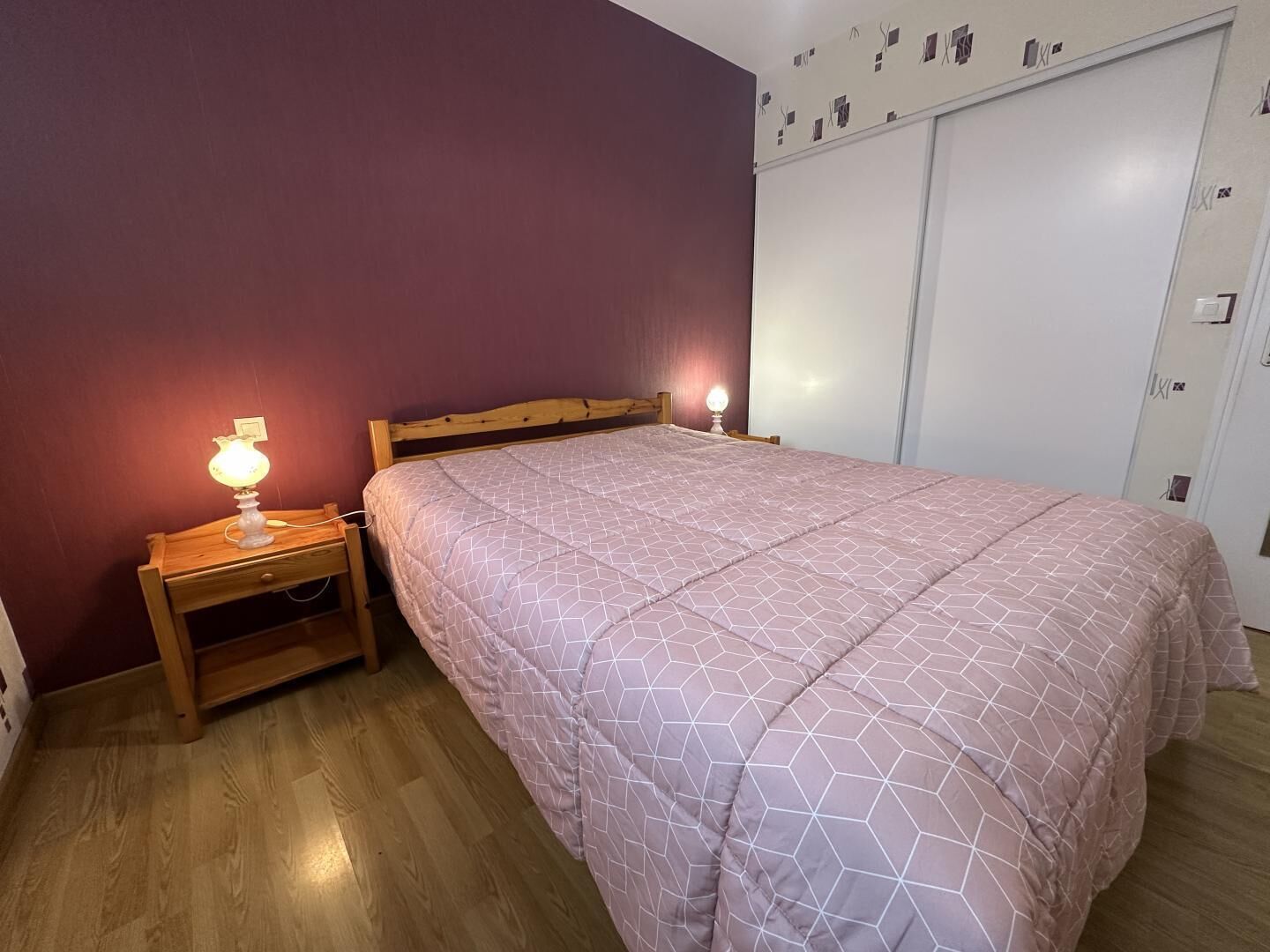 A bedroom with a wooden bed, two bedside lamps, a wooden nightstand, and a wardrobe with a sliding door.
