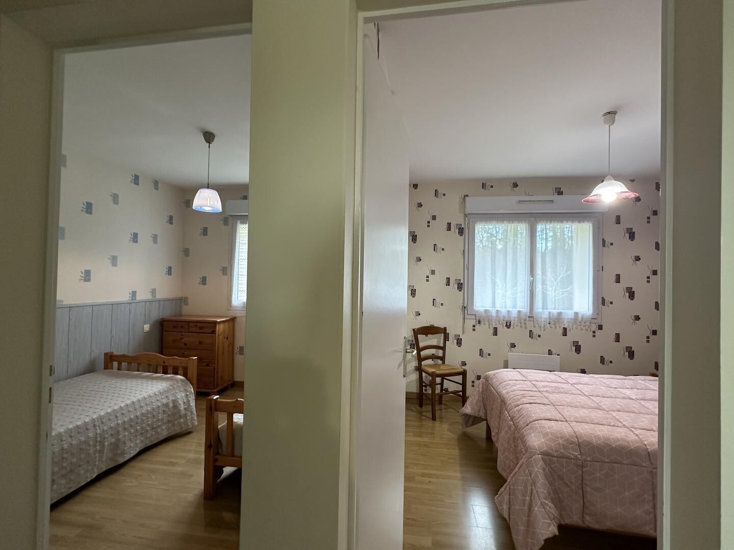 A room with two beds, a wooden chair, a small table, and a window with curtains.