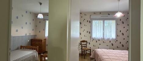 A room with two beds, a wooden chair, a small table, and a window with curtains.