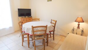 A dining area with a round table, four wooden chairs, a television on a cabinet, and a lamp on a side table. - Chez Michel 1 - Angoume (ANGOUME)