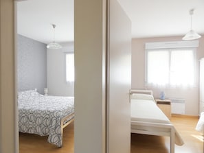 A bedroom with a bed, bedside table, lamp, and window. - Chez Michel 1 - Angoume (ANGOUME)