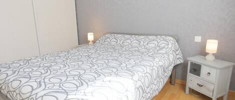 A single bed with a patterned bedspread, a bedside table with a lamp, and a drawer unit.