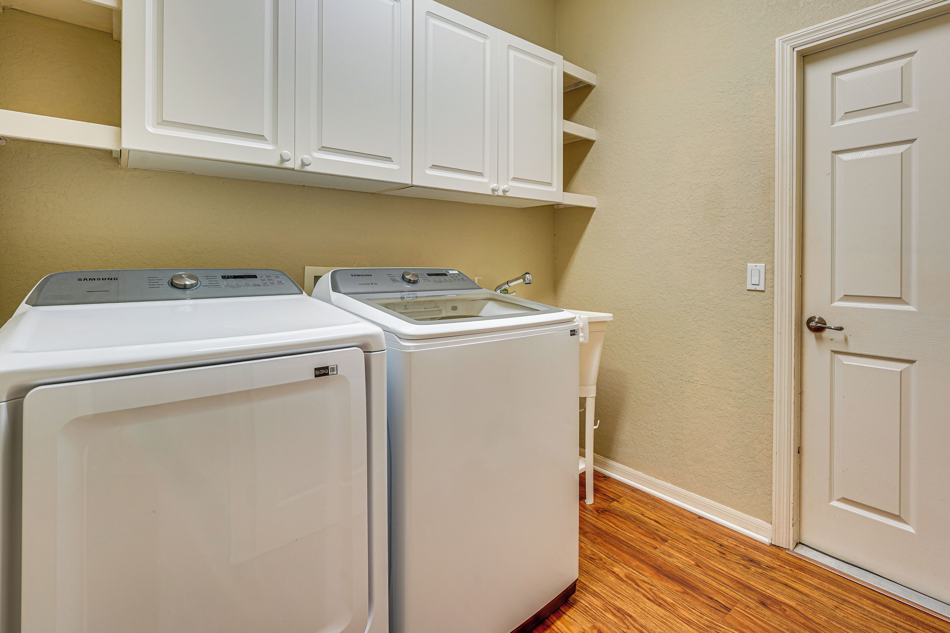 A laundry room with a front-loading washer and dryer, a sink, and a door to the right.
