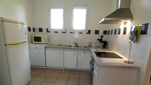A compact kitchen with white cabinets, a microwave, a sink, and a stove. There are two windows providing natural light. - Chalosse - Mugron - Gîte (MUGRON)