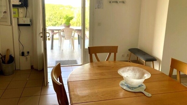 A dining area with a wooden table, chairs, and a bench. There is a window with a view of greenery outside. - Chalosse - Mugron - Gîte (MUGRON)