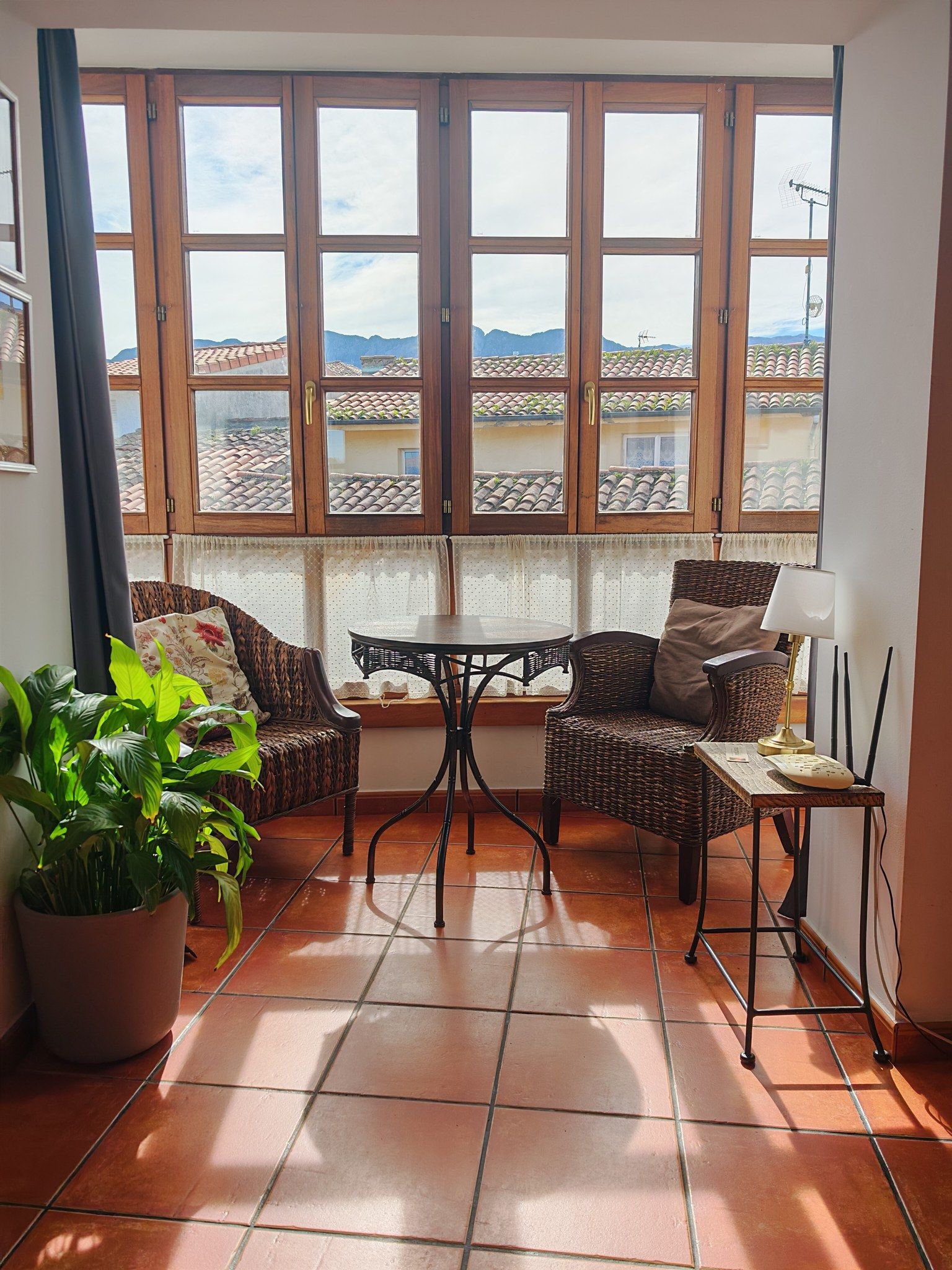 A room with a large window, two wicker chairs, a small table, a potted plant, and a floor lamp.