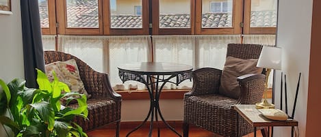 A room with a large window, two wicker chairs, a small table, a potted plant, and a floor lamp.