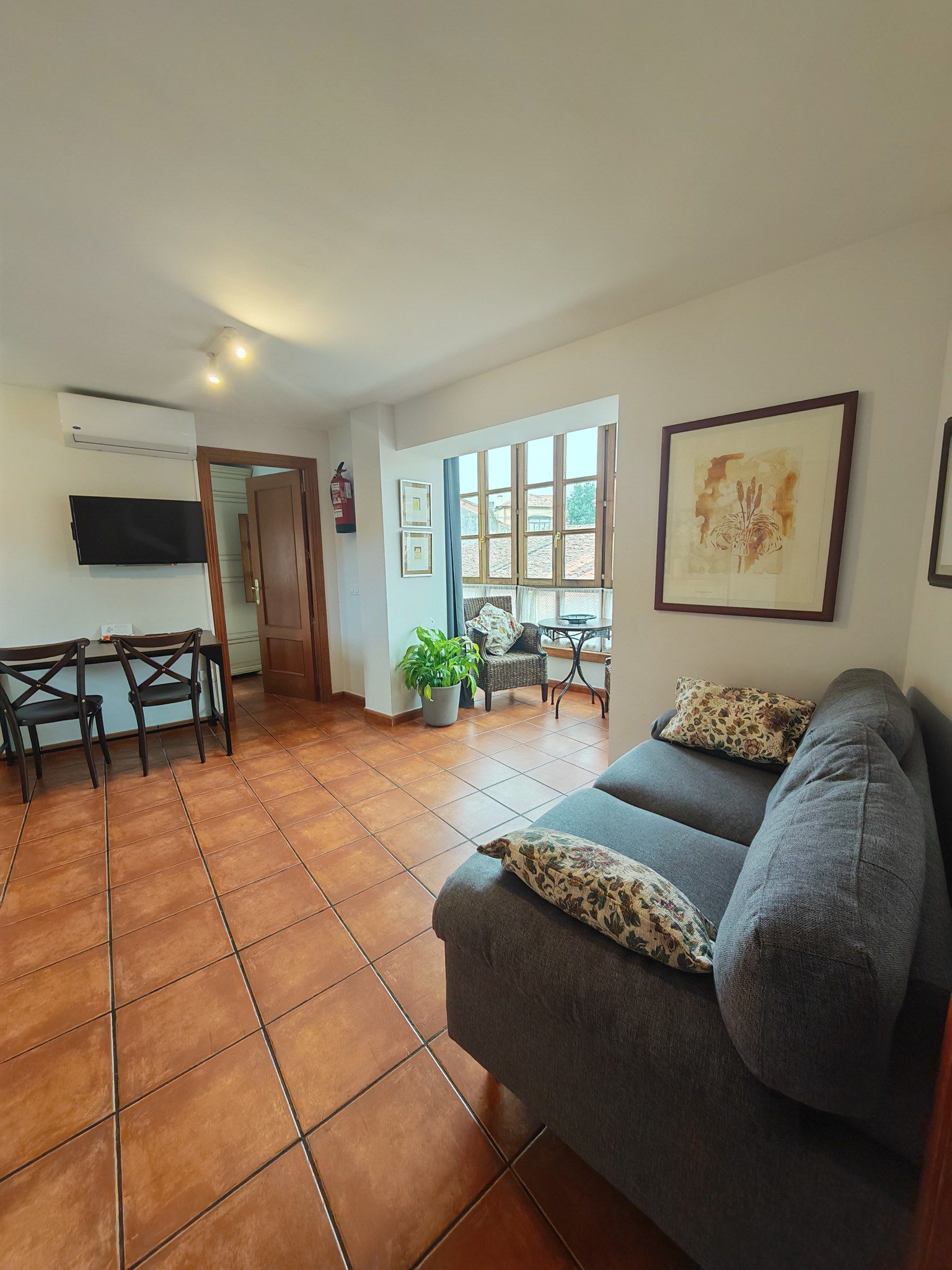 A living room with a sofa, a television, a dining area with chairs, and a window with a view.
