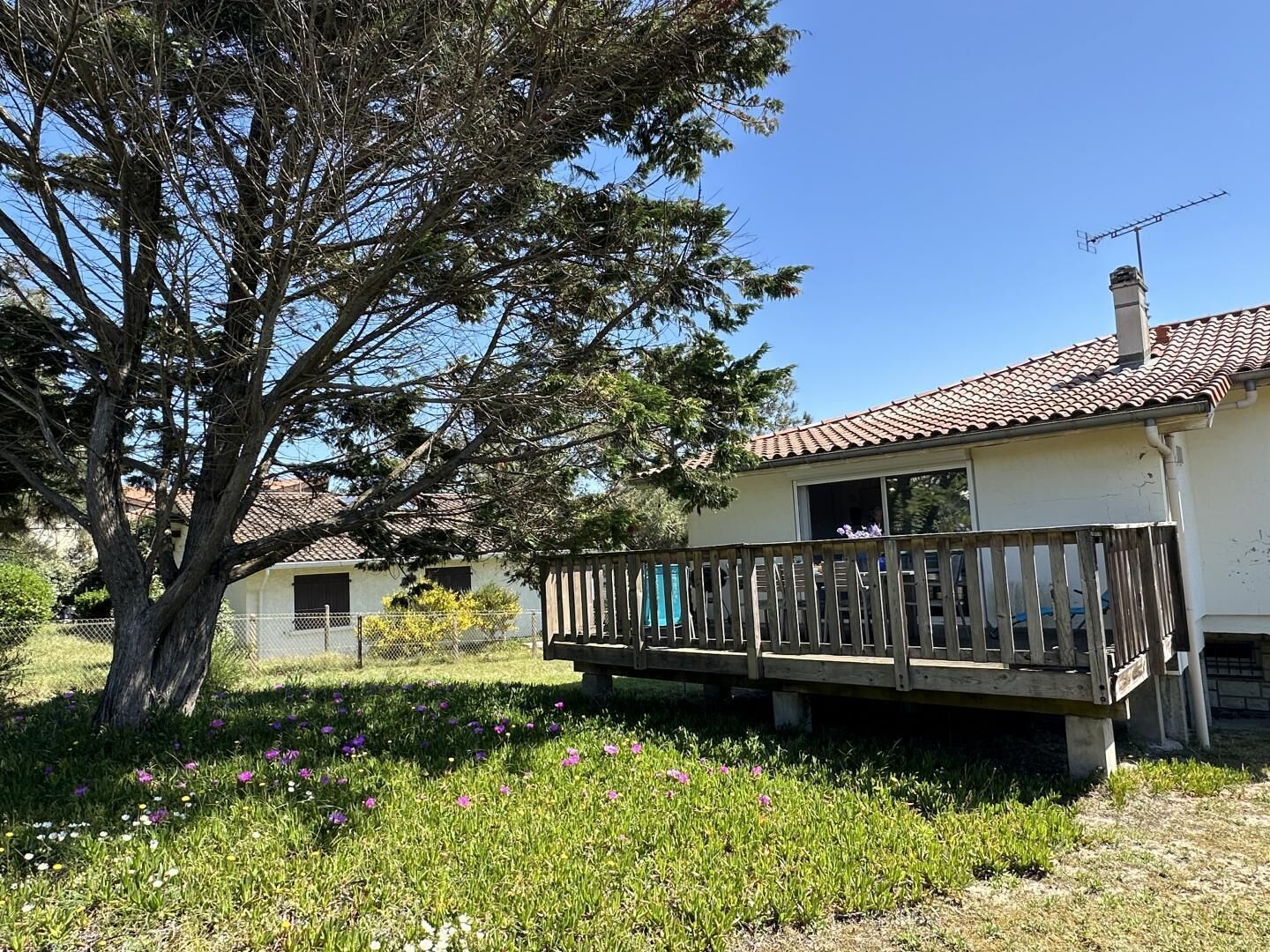 Une maison dotée d’un balcon, entourée d’un jardin où poussent différentes sortes de fleurs.
