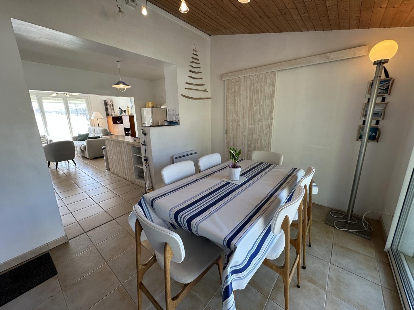 Un coin repas avec une table dressée pour quatre personnes, une cuisine en arrière-plan et une vue sur l’extérieur.
