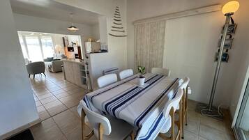 Un coin repas avec une table dressée pour quatre personnes, une cuisine en arrière-plan et une vue sur l’extérieur.