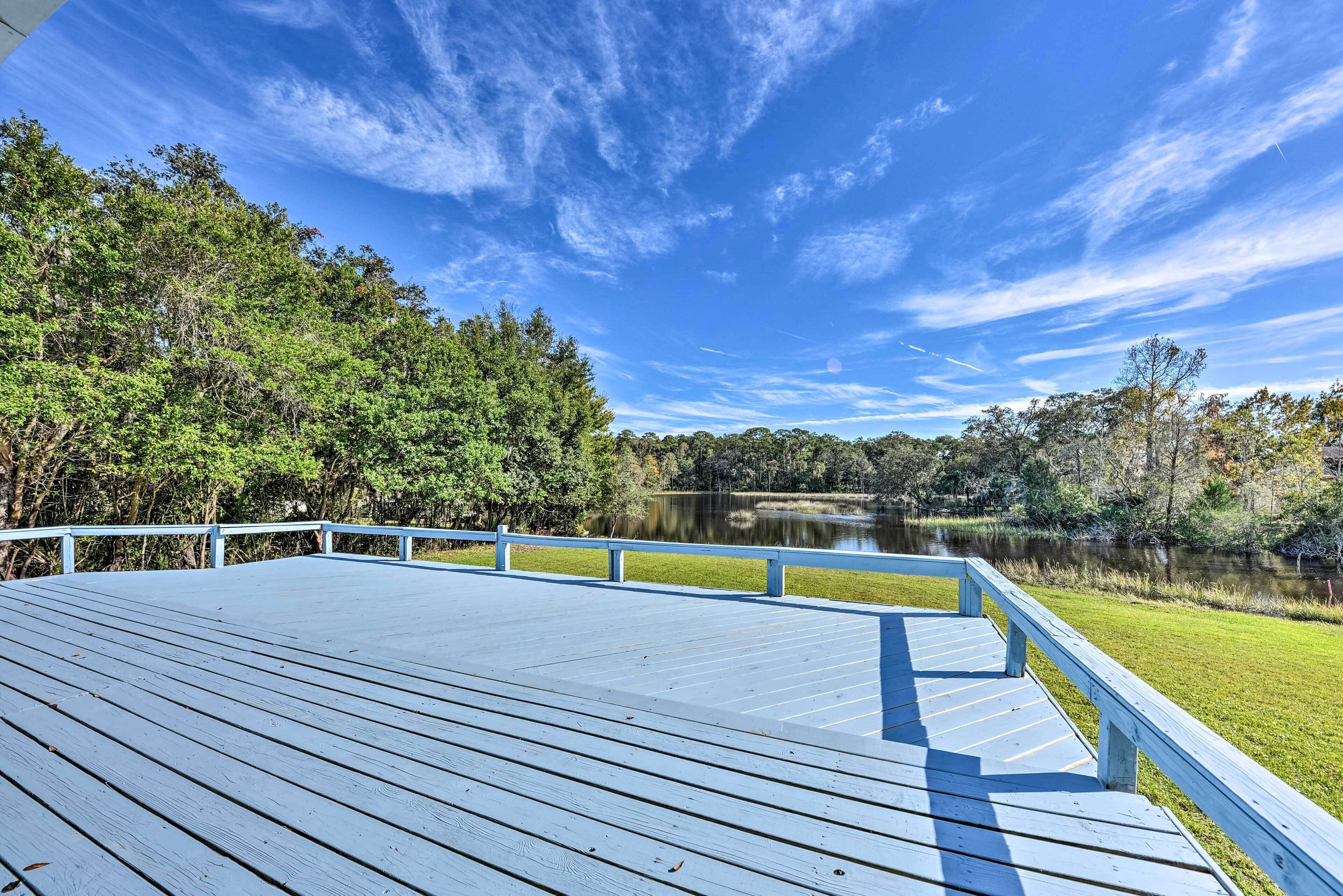 Une terrasse en bois, dotée de rampes de protection, qui offre une vue sur un lac et une zone boisée.
