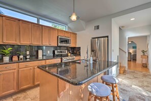 A modern kitchen with wooden cabinets, a central island with bar stools, stainless steel appliances, and a large window providing natural light.