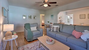 A living room with a grey sofa, a coffee table, and a ceiling fan. There are framed pictures on the wall and a small table with a lamp. - < 9 Mi to Downtown Miami - Modern Getaway (Miami Springs)