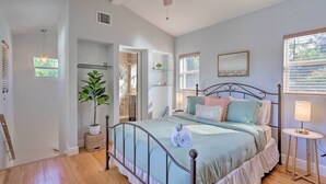A bedroom with a bed, bedside table, lamp, potted plant, and a view of the outside. - < 9 Mi to Downtown Miami - Modern Getaway (Miami Springs)
