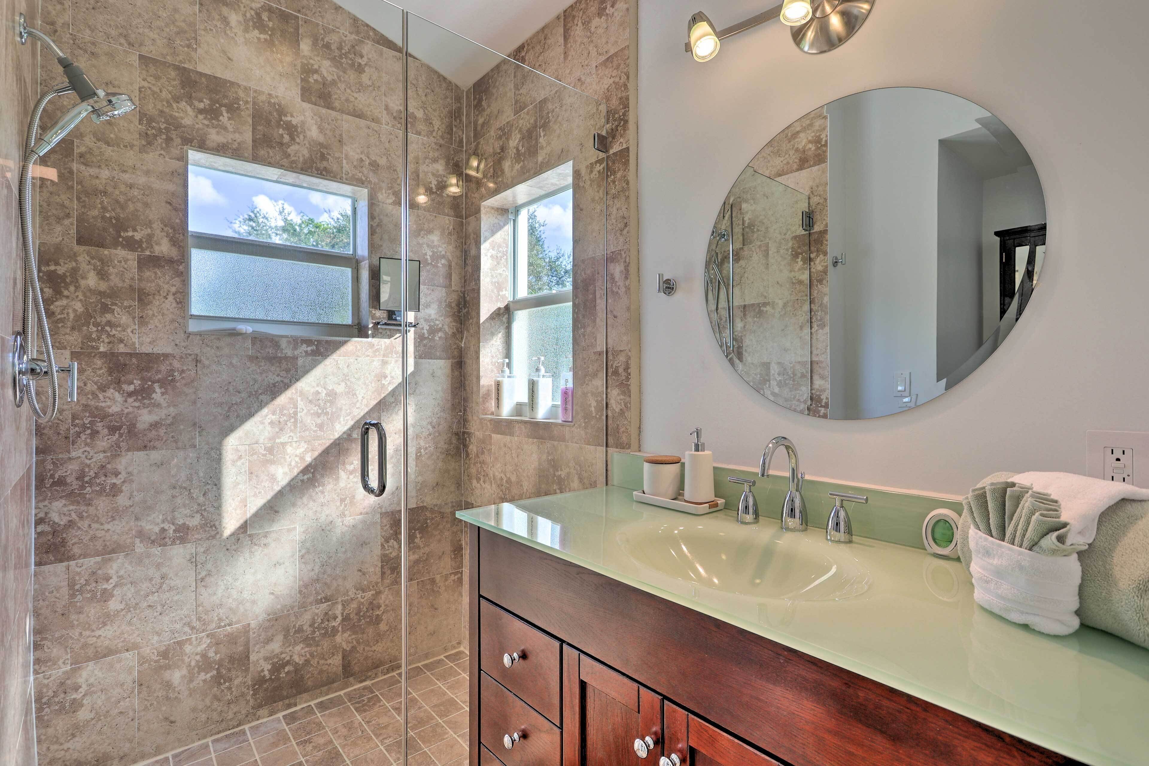 Une salle de bain moderne dotée d’une douche à parois de verre, d’un grand miroir et d’un meuble-lavabo avec un plan de travail vert.