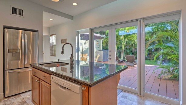 A modern kitchen with a large island, stainless steel appliances, and a view of a patio with outdoor furniture. - < 9 Mi to Downtown Miami - Modern Getaway (Miami Springs)