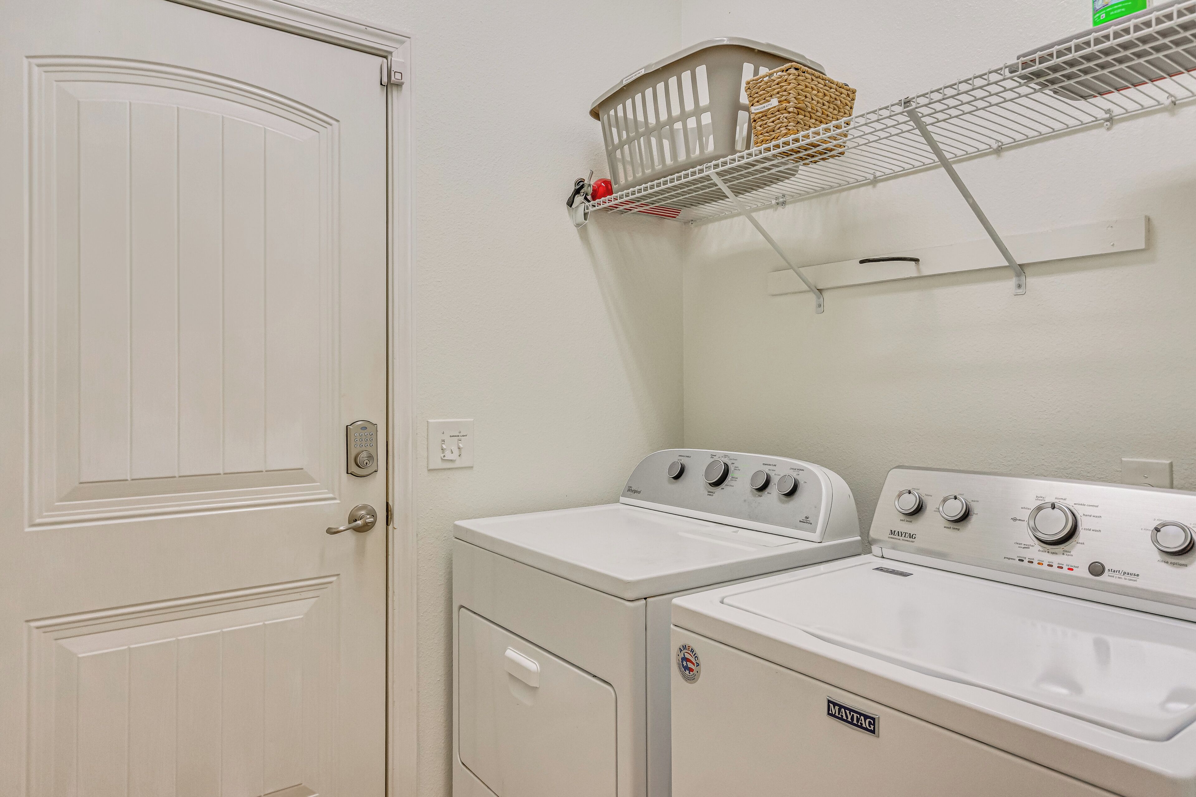 A laundry area with a front-loading washer and dryer, a basket on a shelf, and a door with a keypad lock.