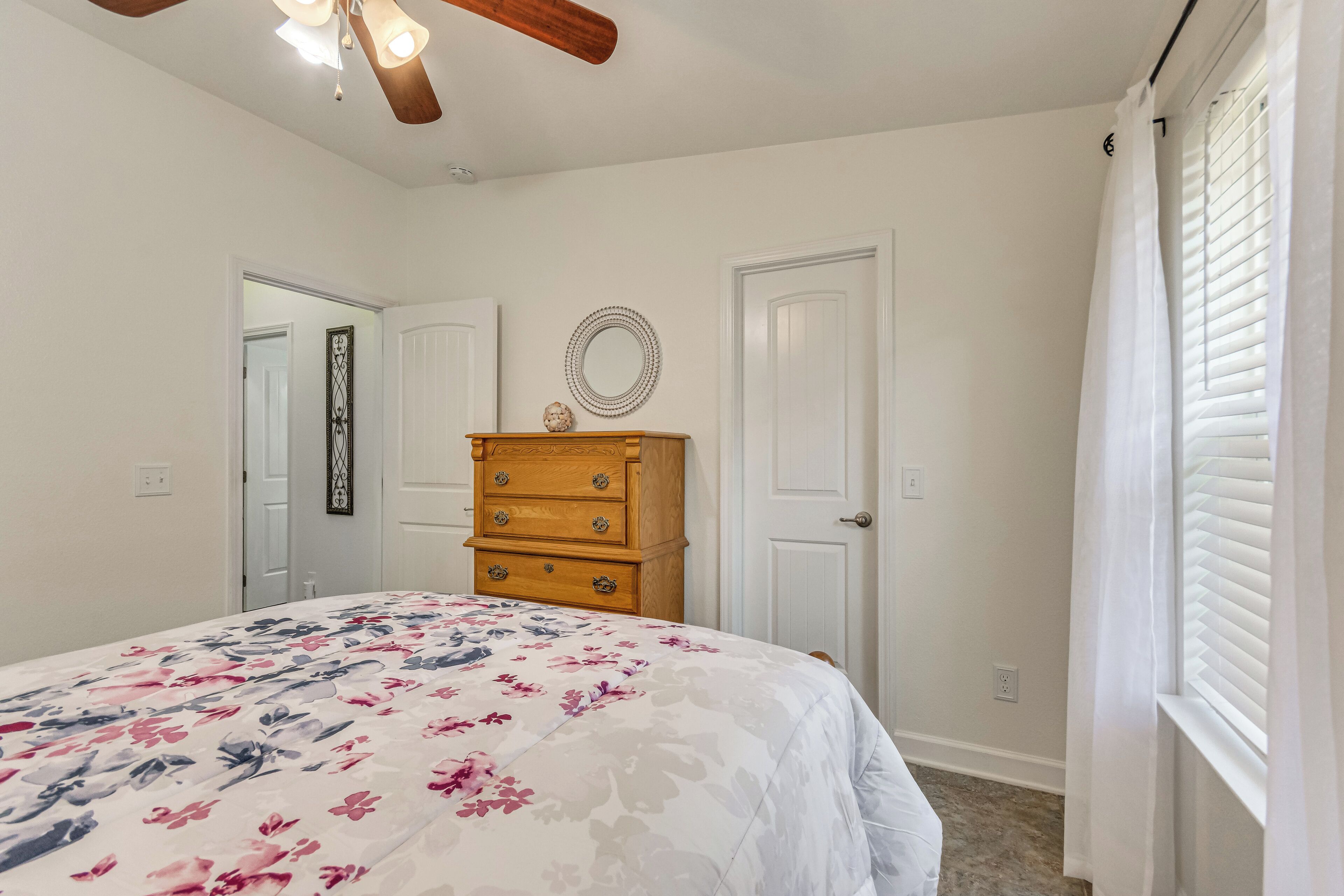 A bedroom with a bed, wooden dresser, white doors, and a ceiling fan.
