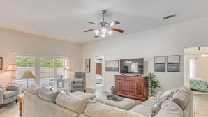 A spacious living room with a large sectional sofa, a ceiling fan, a television, and a dining area with a table and chairs. - Comfortable Pensacola Home w/ Private Pool! (Pensacola)