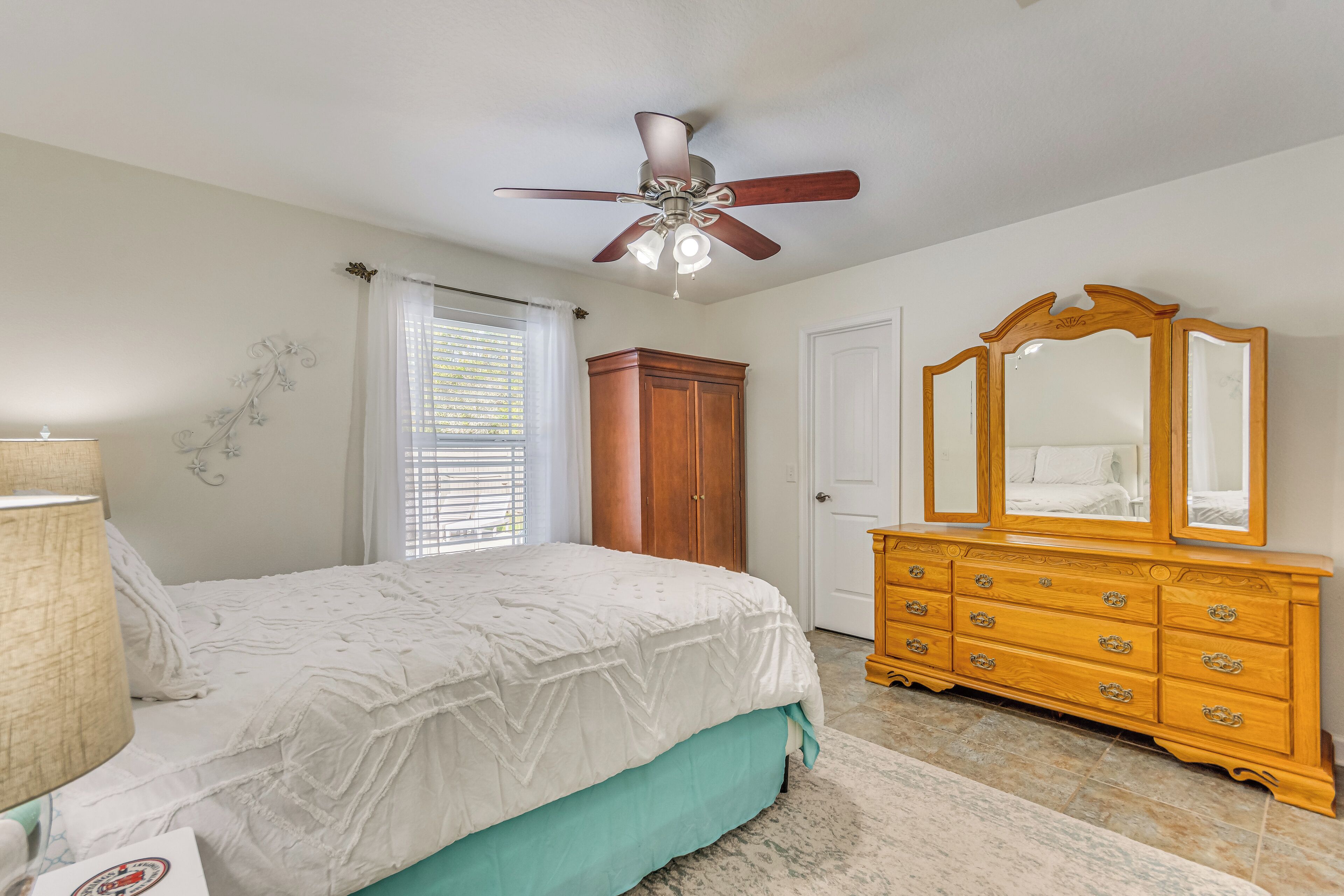 Une chambre à coucher avec un lit, une commode en bois, un ventilateur de plafond et une porte.