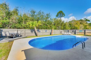 Ein Pool mit gewölbter Kante, umgeben von einem Holzzaun, und eine Terrasse mit Gartenmöbeln.