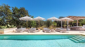 Ein Poolbereich mit Liegestühlen und Sonnenschirmen, umgeben von viel Grün.