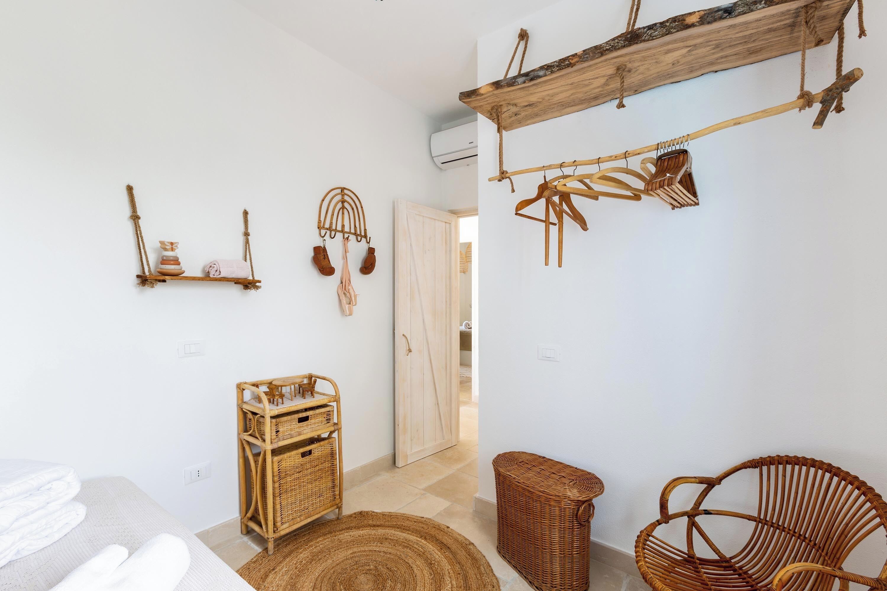 A room with a bed, wicker furniture, a wooden shelf, and a door leading to another room.