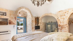 Ein Schlafzimmer mit Steinwänden, einem Bett mit beiger Decke, einem Holzschrank und einem an der Wand montierten Fernseher.
