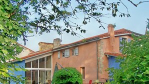 Une maison à deux étages avec une grande baie vitrée au rez-de-chaussée, un petit jardin et une chaise rouge à l’extérieur.