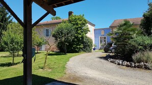 Une allée de gravier mène à un bâtiment doté d’un toit en tuiles et d’une porte bleue.