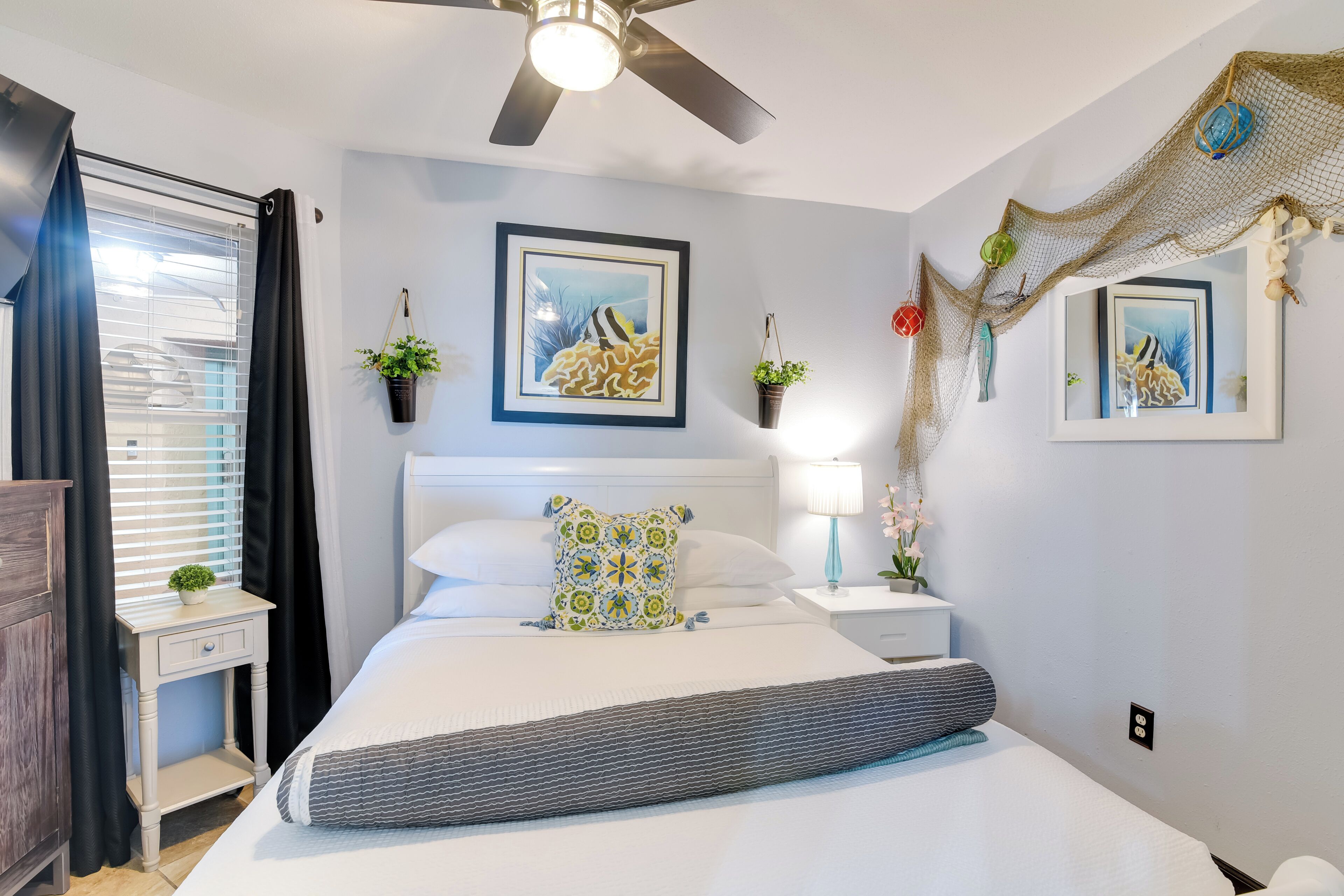A bedroom with a bed, a nightstand, a ceiling fan, and wall-mounted artwork.
